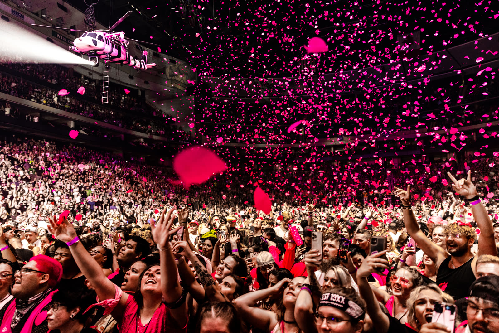 A zebra-striped helicopter hangs over the arena with its searchlight on and ladder down while pink confetti storms over the crowd, Mainstream Sellout tour.